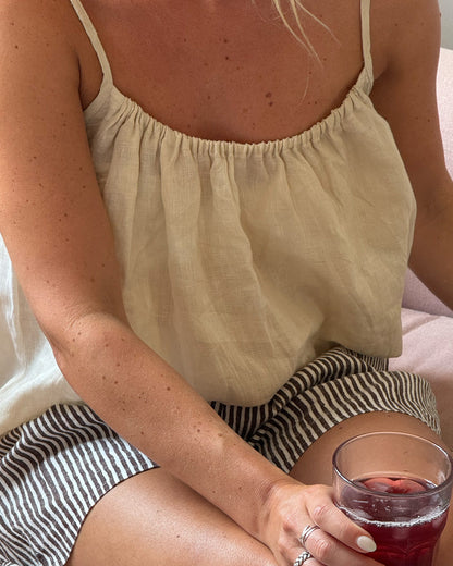 Person wearing a light-colored top and striped shorts, holding a glass of red wine.