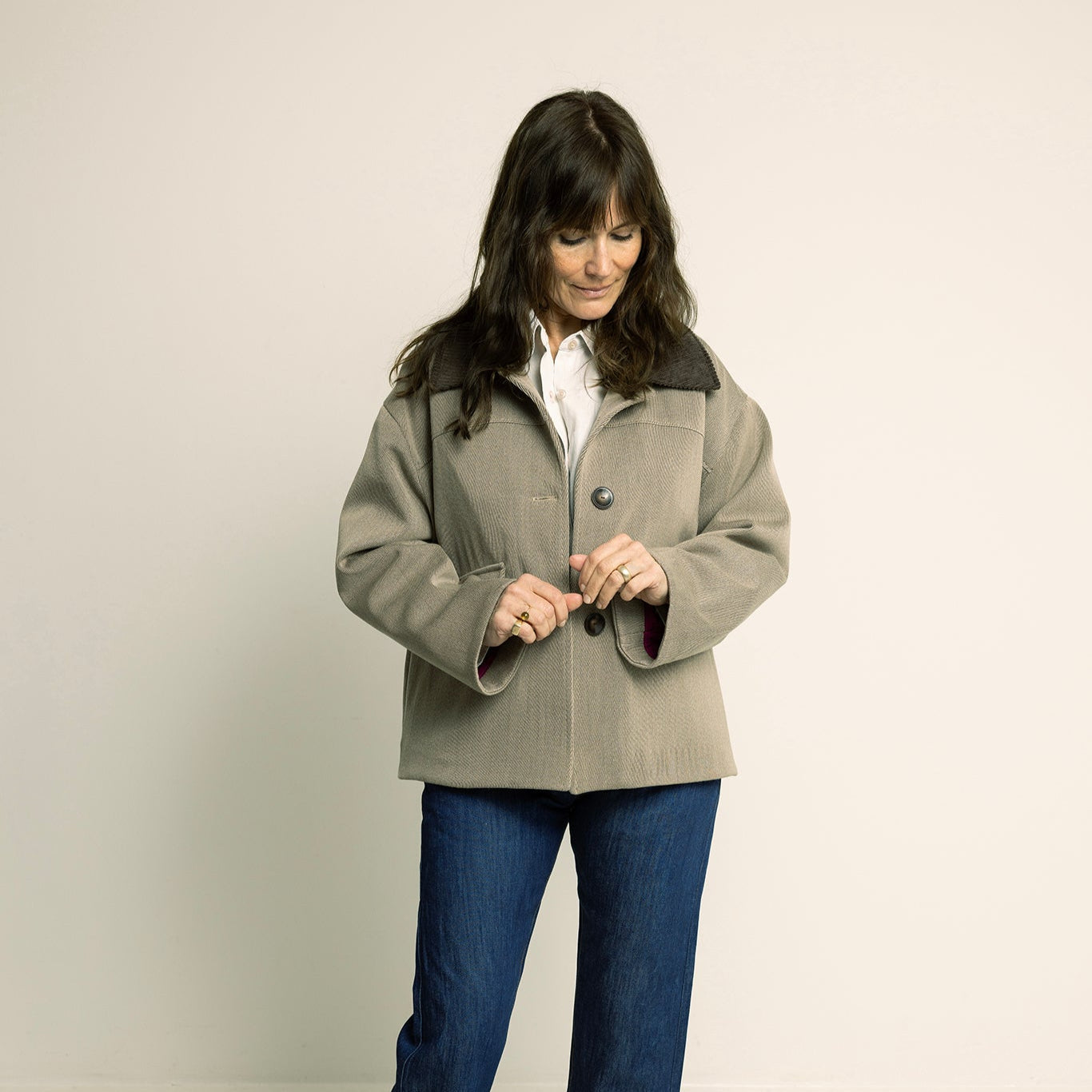 Woman wearing a beige coat and blue jeans on a plain background
