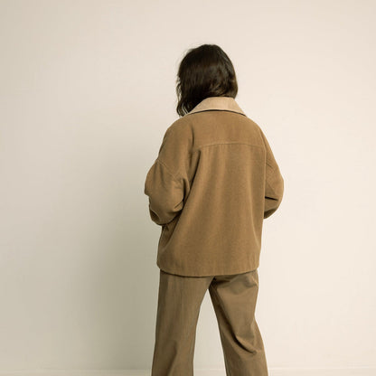 Person wearing a beige suit standing against a plain background