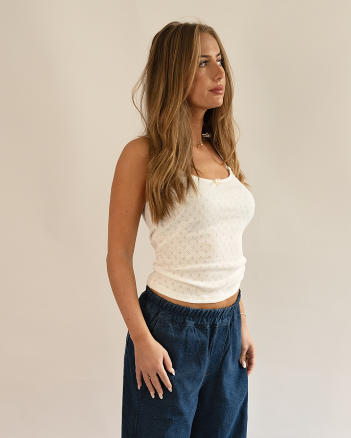 Woman wearing a white top and blue pants against a plain background