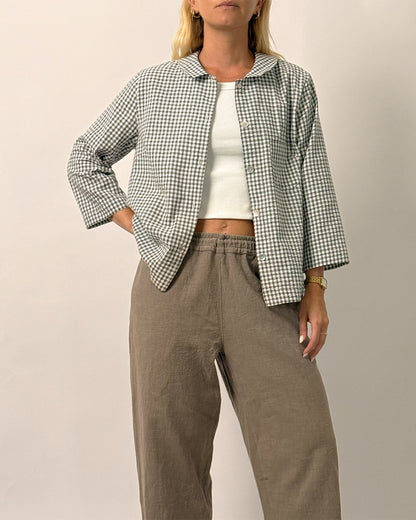 Woman wearing a checkered jacket, white top, and brown pants on a plain background