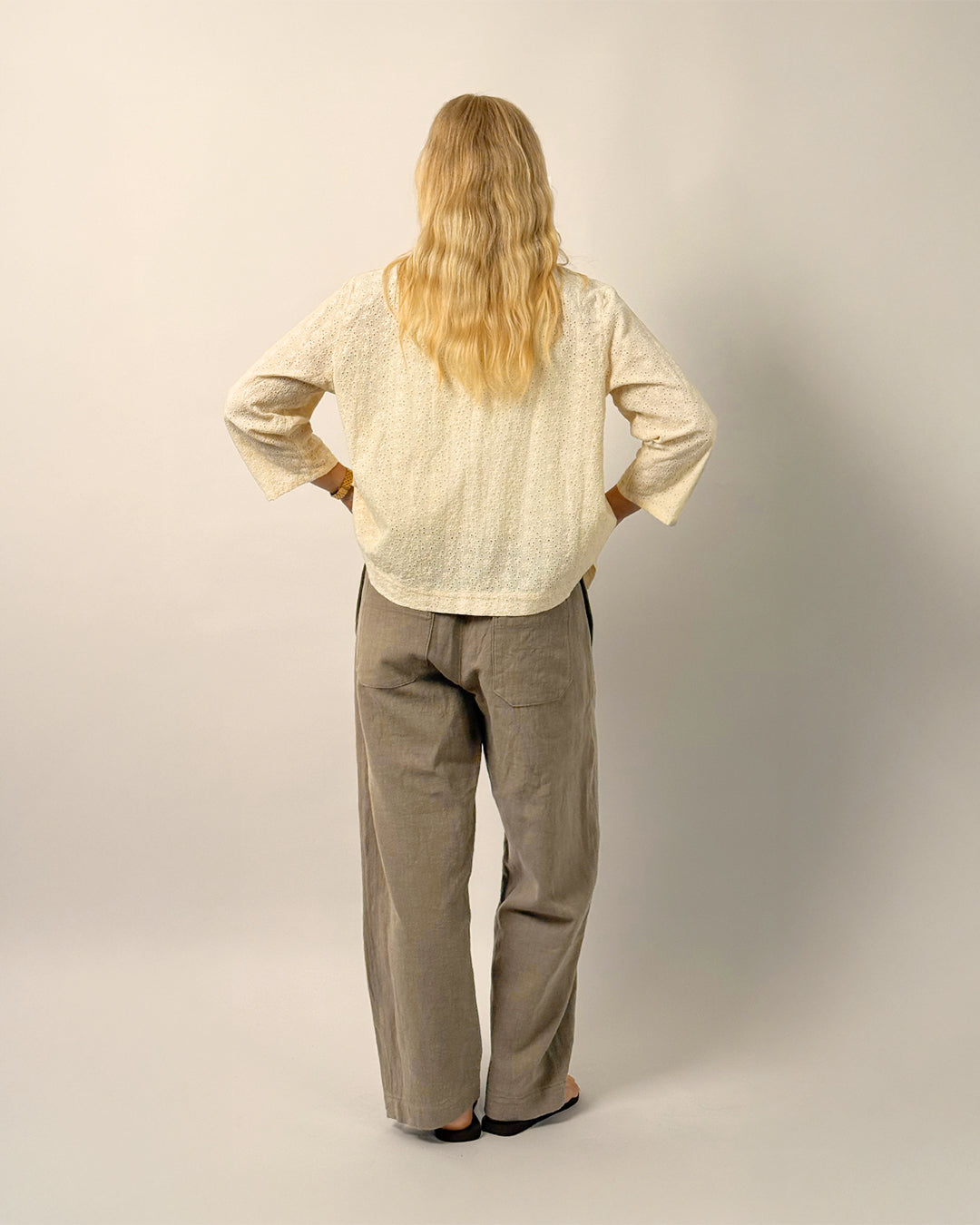 Person wearing a beige shirt and gray pants against a plain background