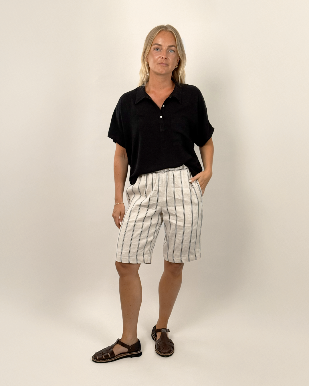Person wearing a black shirt and striped shorts on a plain background