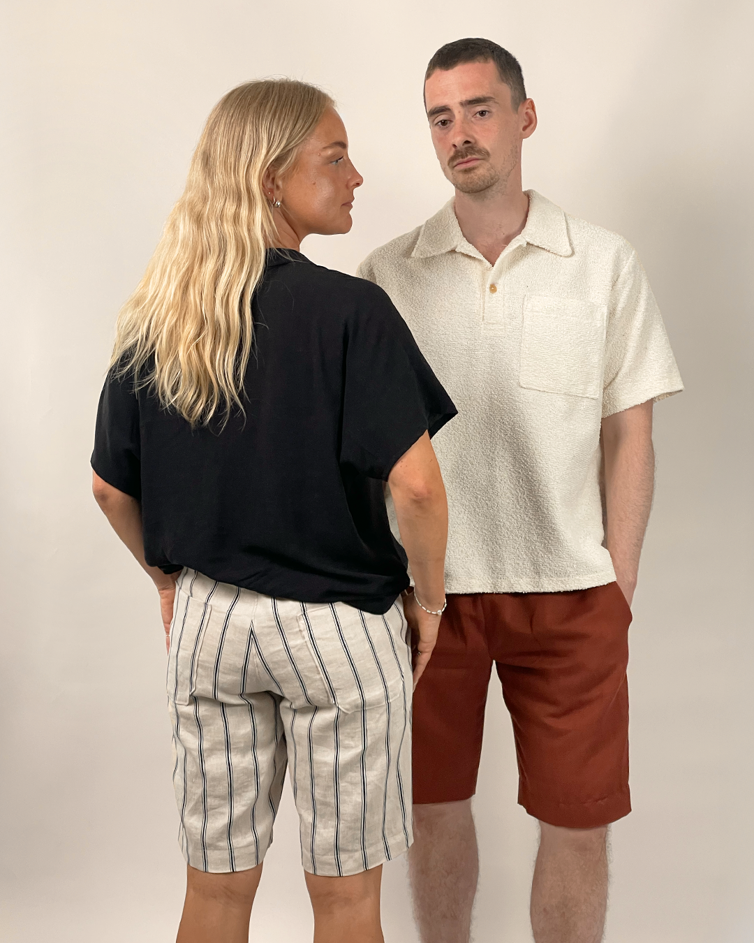 Two people standing side by side wearing casual clothing against a plain background