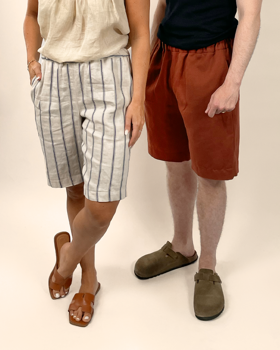 Two people wearing shorts and sandals on a plain background