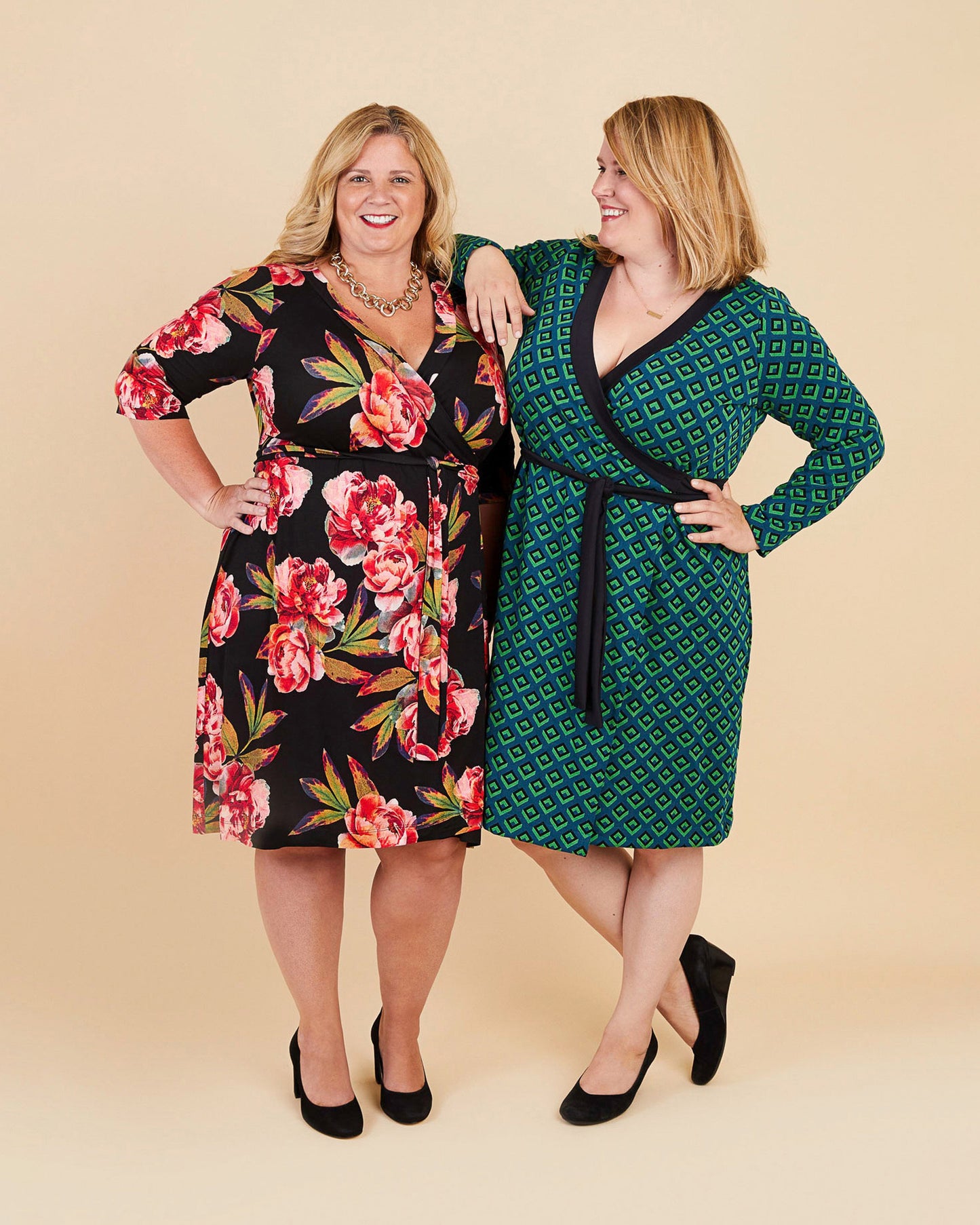Two women wearing floral and patterned dresses on a beige background. This dress is the Appleton Wrap Dress sewing pattern from Cashmerette.
