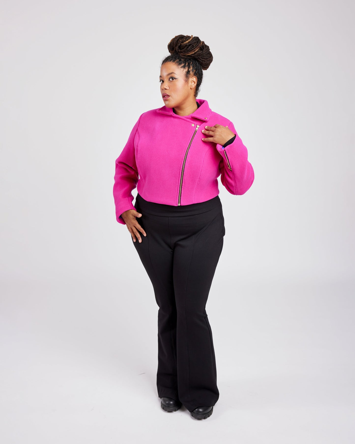 Person wearing a bright pink hoodie with a zipper and black pants on a white background. This biker jacket is the Canton Moto Jacket sewing pattern from Cashmerette.