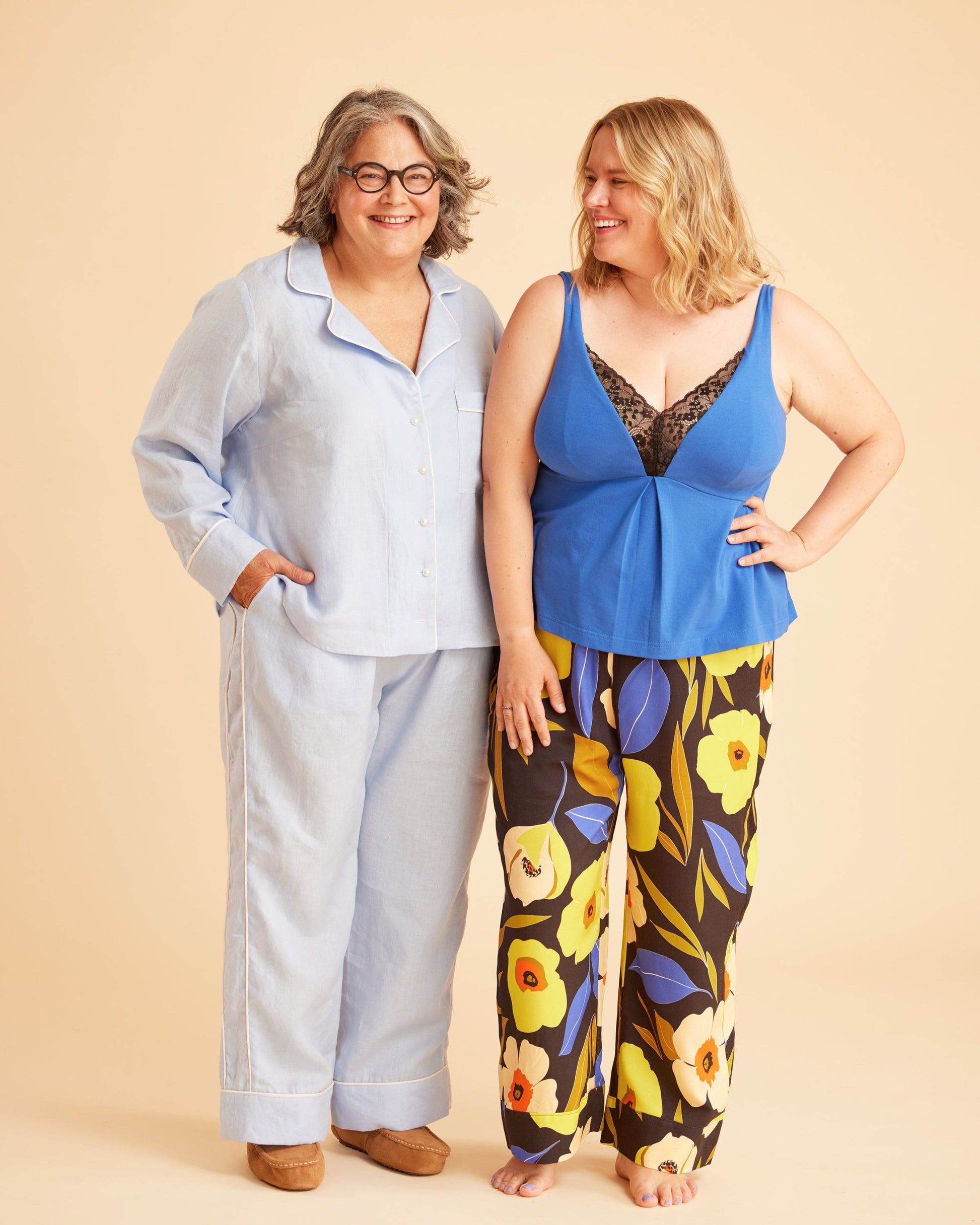Two women standing side by side against a beige background, one in light blue outfit and the other in colorful floral pants. This is the Fiske Sleepwear Set sewing pattern from Cashmerette.