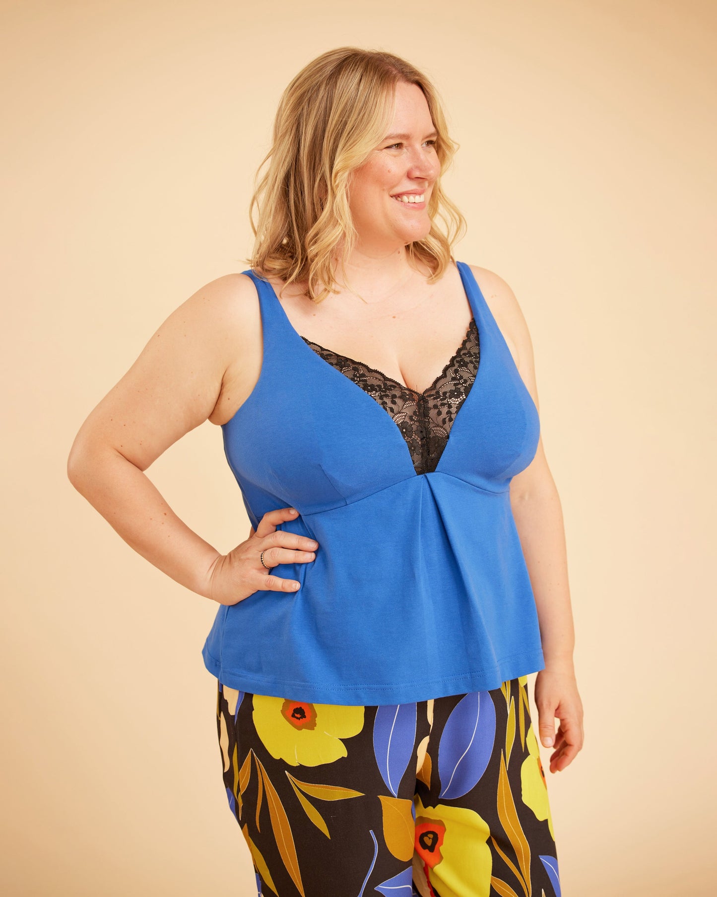 Woman wearing a blue top with floral pants on a beige background. This is the Fiske Sleepwear Set sewing pattern from Cashmerette.