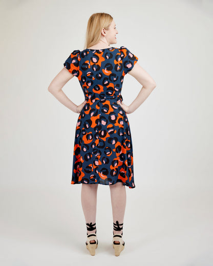 Woman wearing a patterned dress on a plain background. This dress is the Roseclair Wrap Dress sewing pattern from Cashmerette.