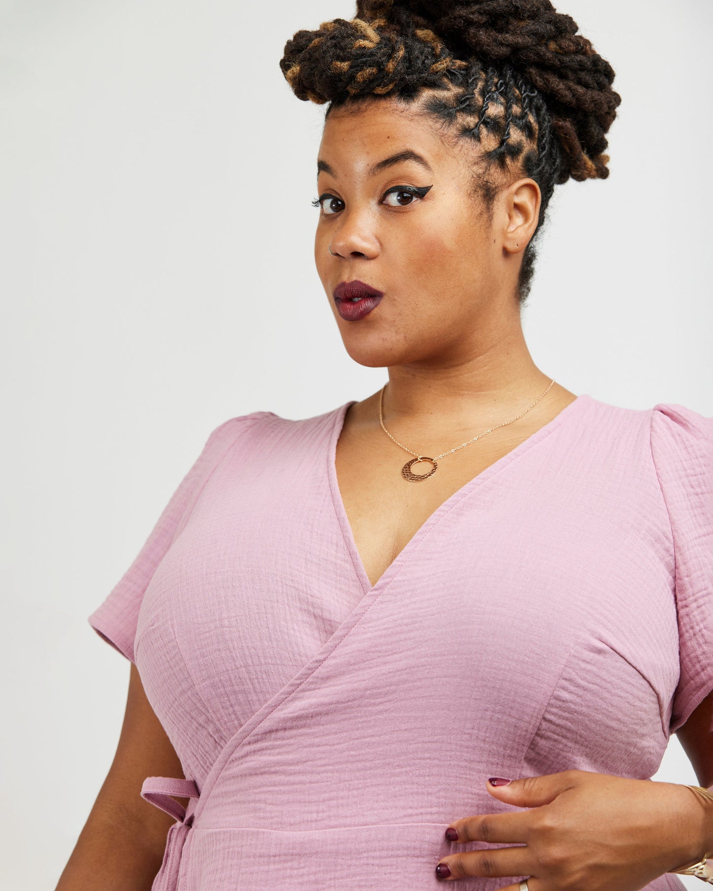 Woman wearing a pink dress against a white background. This dress is the Roseclair Wrap Dress sewing pattern from Cashmerette.