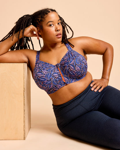 Woman wearing a blue patterned sports bra and navy leggings against a beige background. This is the Cashmerette Somerville Sports Bra sewing pattern for big boobs.