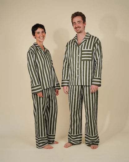 A man and a woman modeling matching striped pajama sets against a plain beige studio background. The pajamas feature vertical stripes in dark green and off-white, with a long-sleeve button-up top and matching pants.