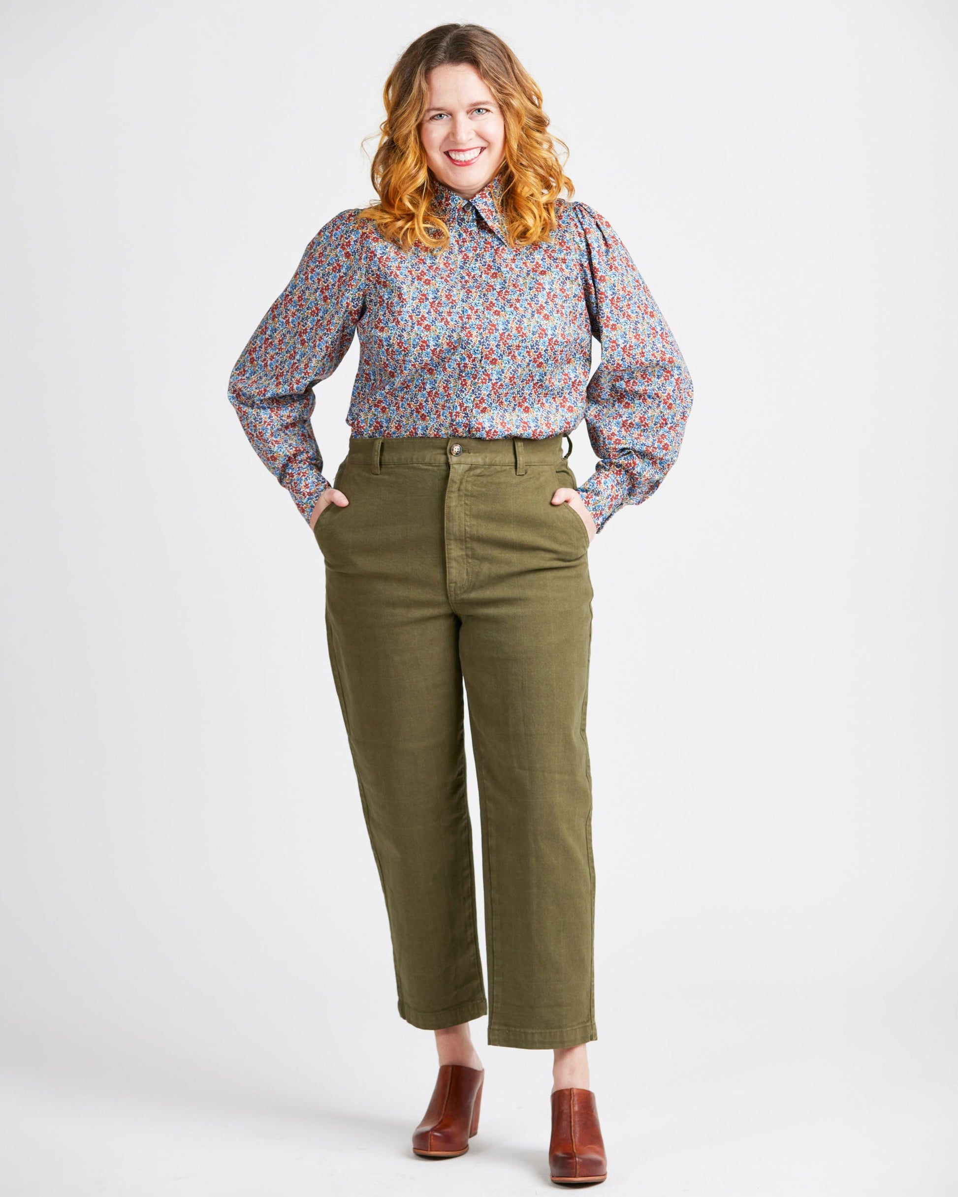 Woman wearing a floral blouse and green pants on a white background. This top is the Vernon Shirt sewing pattern from Cashmerette.